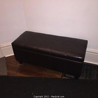 Black leatherette bench with tufted top, placed against a wall on hardwood floor.