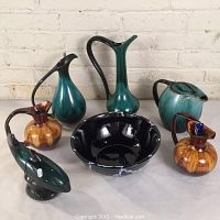 Full view of all Blue Mountain Pottery items including pitchers, bowl, and whale-shaped dish arranged on table against brick wall.