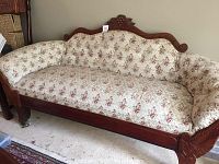 Full view of the vintage settee showing its floral upholstery and carved wooden base on carpeted floor.