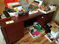 Full view of the Belair wooden office desk showing the top surface and drawer area with various items stored on and under the desk.