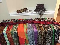 Full view of 17 scarves laid out showing various colors and patterns including animal prints and solid colors, with purses positioned behind.