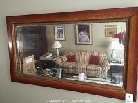 Full view of rectangular wooden framed mirror hanging on wall reflecting a living room.