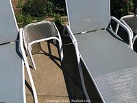 Photo showing a close-up of another side of a lounge chair and the glass top side table beside it, outdoors on a concrete surface.
