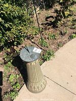 Concrete sundial on a corinthian column style base sitting in garden soil near a path.