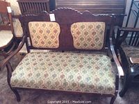 Front view of carved wooden settee with floral tapestry upholstery