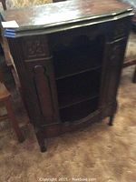 Front and side view of the dark wooden antique display cabinet showing carved detailing and three shelves.