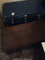 Closed view of blue metal chest and wooden chest side by side on floor.