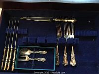 Top view of silverware with knives, forks, and spoons arranged in velvet-lined compartmented chest.