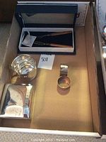 Photo showing four silver items arranged in box: silver cigarette box, silver cup, silver napkin ring, and boxed fork and knife set with wooden handles.