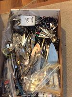 Top-down view of box containing assorted flatware and serving utensils.