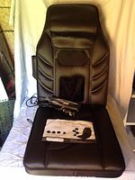 Full view of black massage seat cushion with remote control device and instruction pamphlet on seat surface.