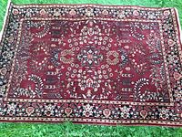 Full view of wool area rug spread on grass showing the overall red background with floral and leafy patterns.