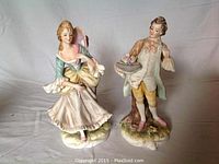 Both bisque figurines standing side by side, showing full view of the figures and bases