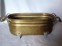 Front-side view of the brass flower pot showing overall shape and condition, including feet and handles.