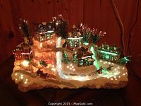 Front angle view of the Christmas village showing lit houses, snowy landscape, sledding figurines, and trees.