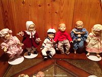 Six Ashton Drake collectible dolls arranged in a row, showcasing various costumes and expressions.