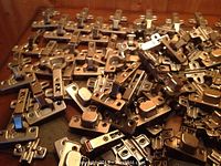 Multiple new metallic cabinet door hinges piled together.