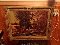 Full frontal view of framed landscape print leaning against wood‐paneled wall