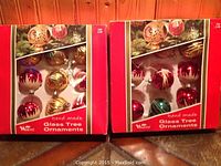 Two unopened Woolcrest handmade glass ornament sets in original red/white boxes, sealed and intact.