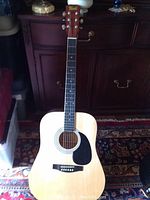 Full front view of natural wood acoustic guitar with black pickguard on a carpeted area