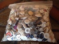 Photo of a clear zip-lock bag filled with various vintage buttons predominantly in white and cream shades with some darker and colored ones mixed in.
