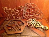 Set of four brass decorative stands on wooden surface, displaying butterfly, pineapple, hexagonal floral, and geometric designs