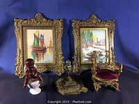 Photo showing the full lot including two framed miniature oil paintings, ceramic figurine, bronze ashtray, and miniature ornate chair arranged together on blue fabric background.