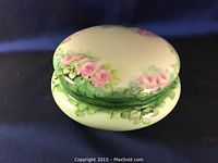 Top and angle view of oval Limoges porcelain trinket box showing hand-painted pink roses and green leaves on lid and base.