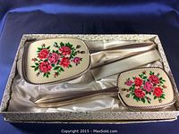 Closed view of three-piece vintage vanity set in original box with floral print on brush and mirror.
