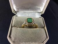 Ring set in open grey velvet box showing emerald and clear stone accents