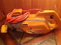 View of the full chainsaw showing the orange body, handle, power cord and plug