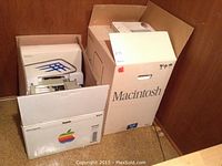 Three cardboard boxes labeled Macintosh and Apple ImageWriter arranged in a wooden cabinet