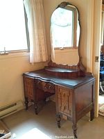 Full view of the wooden vanity dresser sitting near window with lace curtains, showing overall shape, drawers, and attached mirror.