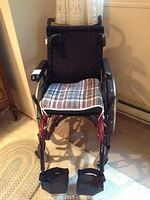 Front view of Parsons ADL carbon wheelchair showing padded black backrest, plaid seat cushion, armrests and footrests.