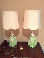 Full view of both lamps showing porcelain bases shaped as female figurines in green dresses and fabric lampshades with scalloped edges.