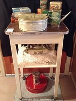 Full view of white wooden side table with multiple collector tins on top and crocheted items on shelf below