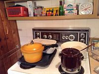 Yellow Westbend pressure cooker, brown fondue pot, cast iron pans on stove