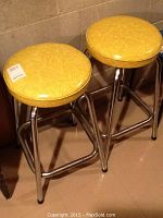 Front and side view of both yellow vinyl bar stools showing overall appearance and pair configuration
