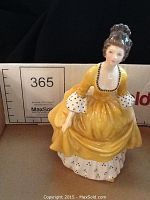 Front view of Royal Doulton Coralie porcelain figurine in yellow dress with detailed white petticoat with black spots.
