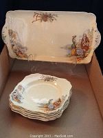 Rectangular serving platter with four matching smaller plates stacked below, all with scenic and floral decorations and gold trim.