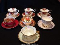 Overview of seven tea cup and saucer sets on black background