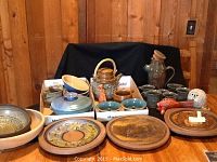 Overview image showing multiple pottery items including bowls, platter, decanter, mugs, and ceramic figurine arranged on table.