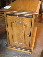 Front view showing oak end table with cupboard door with detailed panel and brass knob.