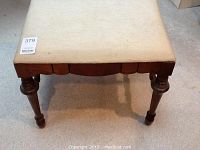 Top front view of the bench showing the beige fabric seat and carved wooden legs.