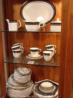 Display cabinet shelf showing 13-inch serving plate, gravy boat, cream pitcher, sugar bowl, and stacked cups and saucers