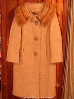 Full front view of the beige women's coat with fur collar hanging on a wooden door.