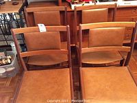 Front view of 4 teak dining chairs with light brown vinyl upholstery.