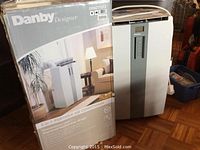Danby Designer 3-in-1 portable air conditioner unit shown next to original box on hardwood floor.