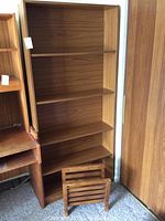 Photo showing a tall wooden bookcase with five shelves and a small wooden slatted magazine rack positioned in front of it.