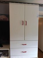 White highboy dresser with two doors closed showing red handles on doors and two drawers below.